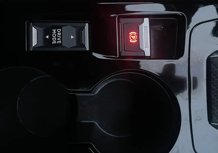Gros plan sur la console centrale noire du Peugeot 208 électrique 2023, avec bouton Drive Mode et frein à main électronique allumé.
