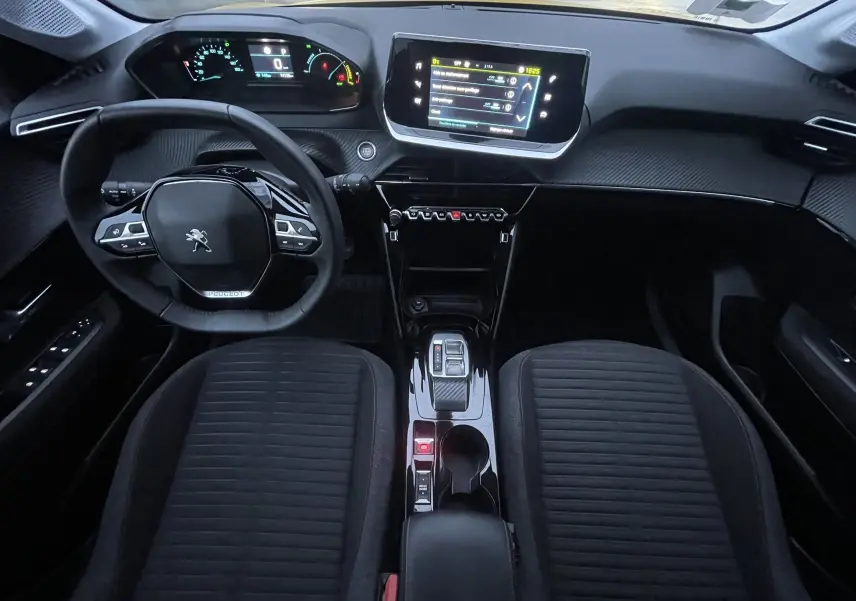 Vue intérieure frontale du tableau de bord et console centrale de la Peugeot 208 II électrique 2023 avec volant compact et écran tactile.