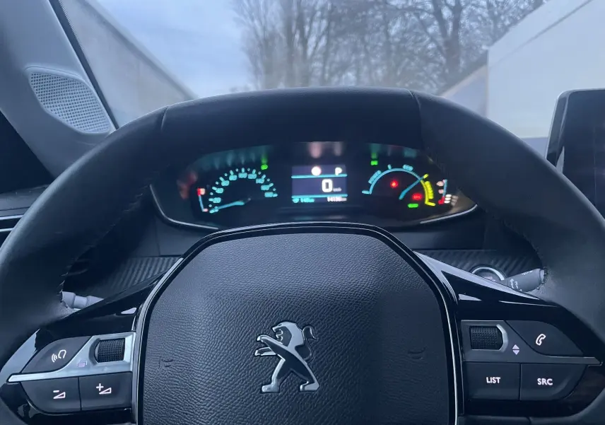 Vue intérieure du volant Peugeot 208 électrique 2023 avec tableau de bord numérique allumé et commandes au volant visibles.