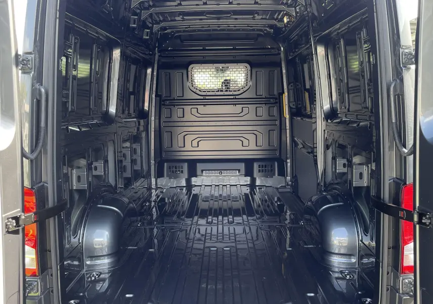 Intérieur du coffre ouvert d'un Volkswagen Crafter gris Indium, montrant la cloison avec vitre fixe et l'espace de chargement vide.