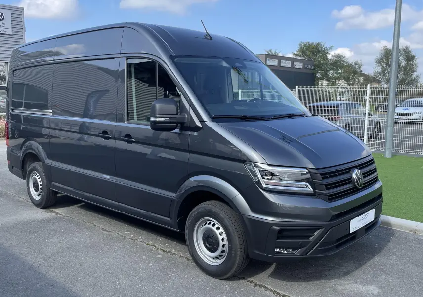 Vue 3/4 avant d'un Volkswagen Crafter Van gris Indium avec phares LED et jantes acier, stationné devant un concessionnaire.