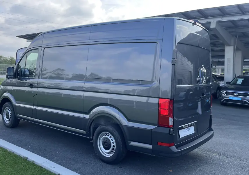 Volkswagen Crafter Van gris Indium vu en 3/4 arrière droit, avec vitres arrière teintées et feux rouges visibles.