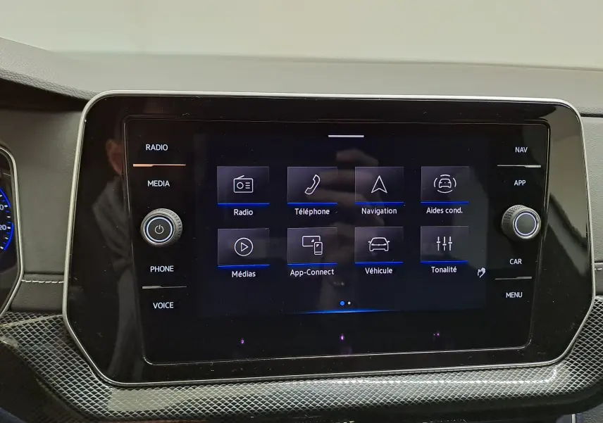 Écran tactile central du Volkswagen T-Cross blanc, affichant le menu principal avec options radio, navigation et véhicule.