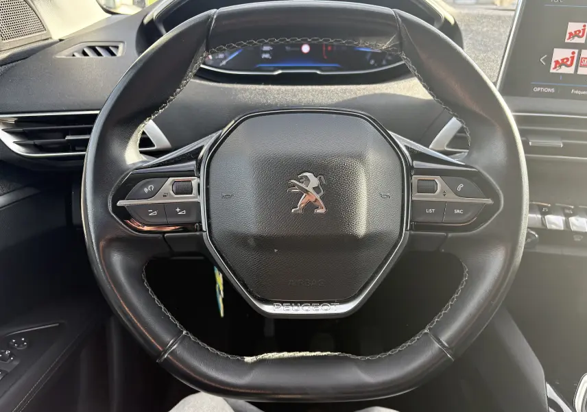 Vue rapprochée du volant en cuir noir du Peugeot 3008 II 1.5 BlueHDi 2019 avec commandes intégrées et tableau de bord numérique.