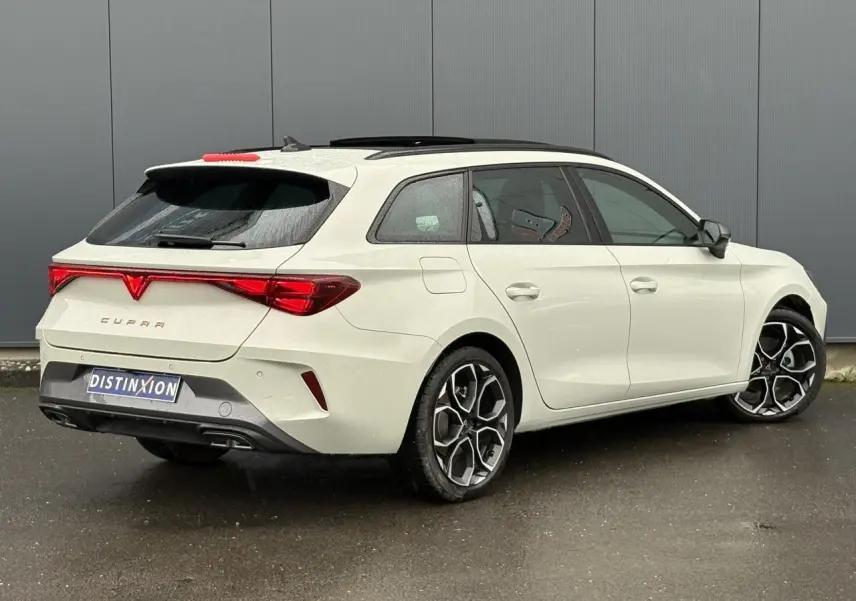 Vue 3/4 arrière droite d'une CUPRA Leon ST 2025 blanche avec toit noir et jantes alliage distinctives.