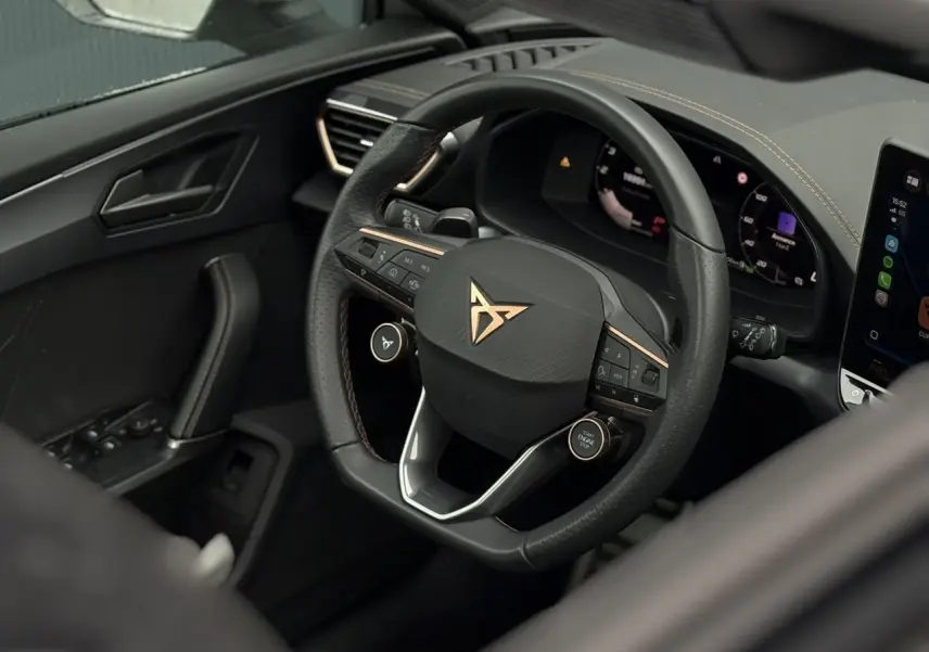 Vue rapprochée du volant CUPRA noir avec logo cuivré et tableau de bord numérique du Leon ST 2025.