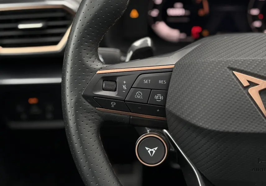 Gros plan sur le volant perforé noir avec logo CUPRA cuivré et commandes intégrées, intérieur moderne et élégant.