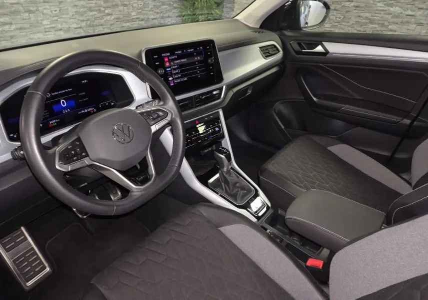 Vue intérieure côté conducteur du Volkswagen T-Roc 2025, avec tableau de bord digital et sellerie tissu noir et gris.