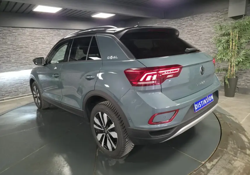 Vue 3/4 arrière droit d'un Volkswagen T-Roc bleu métallisé avec toit noir et badge "GOAL" sur le montant arrière.