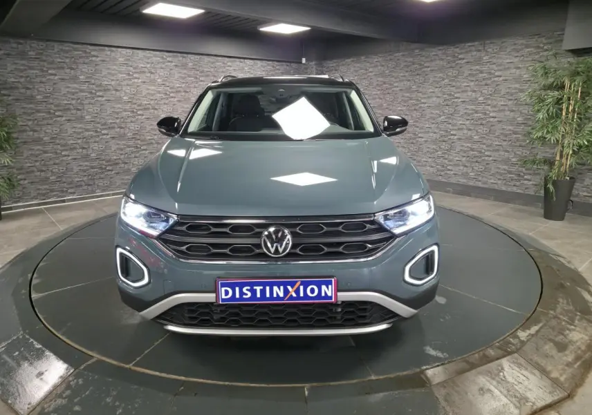 Volkswagen T-Roc bleu en vue frontale, avec calandre noire et feux LED allumés dans un showroom.