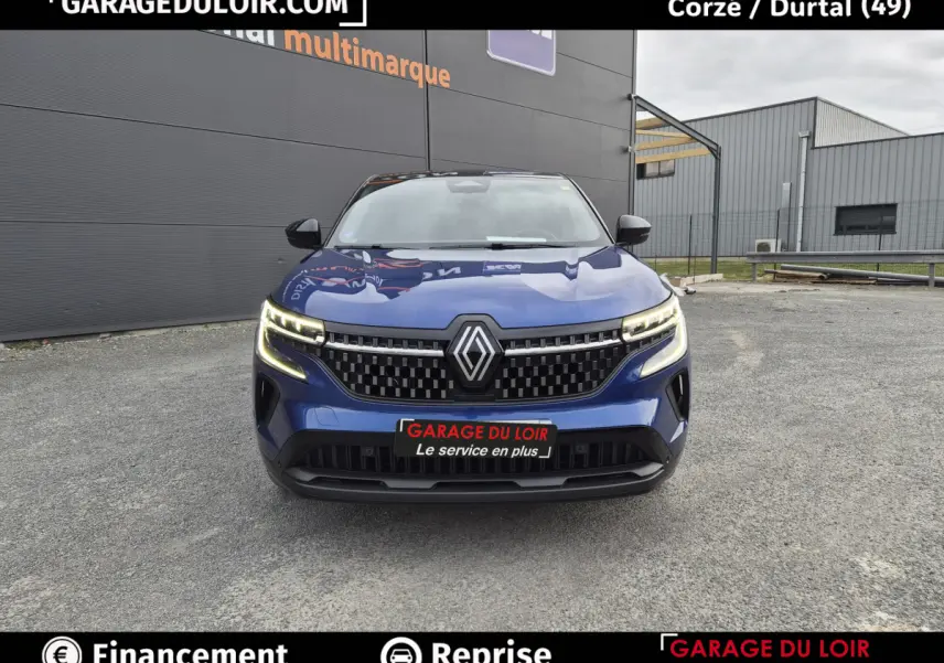 Vue avant d'un Renault Austral bleu avec calandre noire à damier et feux LED allumés sur parking extérieur.