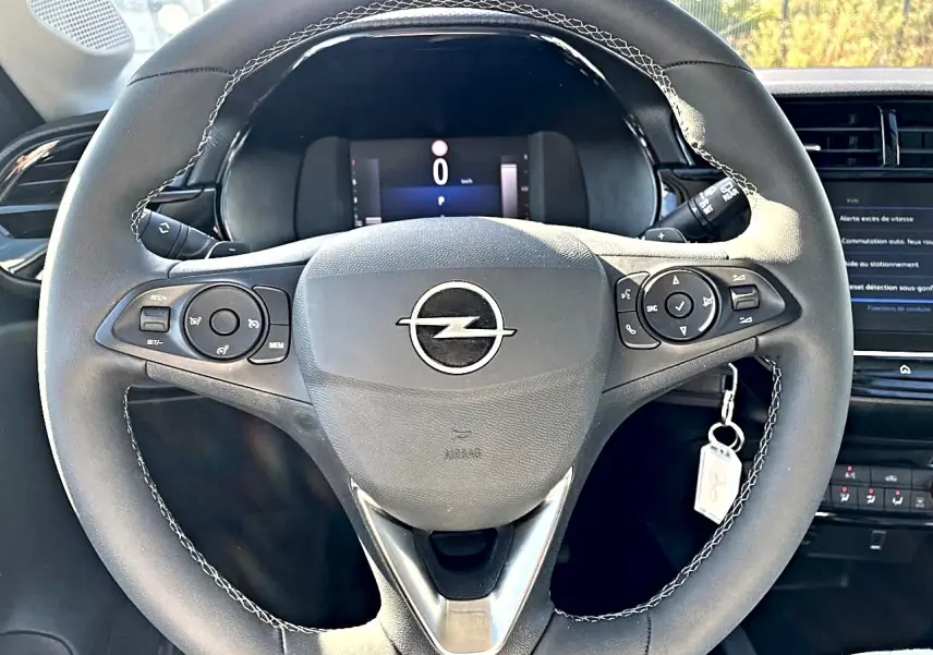 Vue frontale du volant sport noir avec surpiqûres blanches et logo Opel au centre du tableau de bord gris.