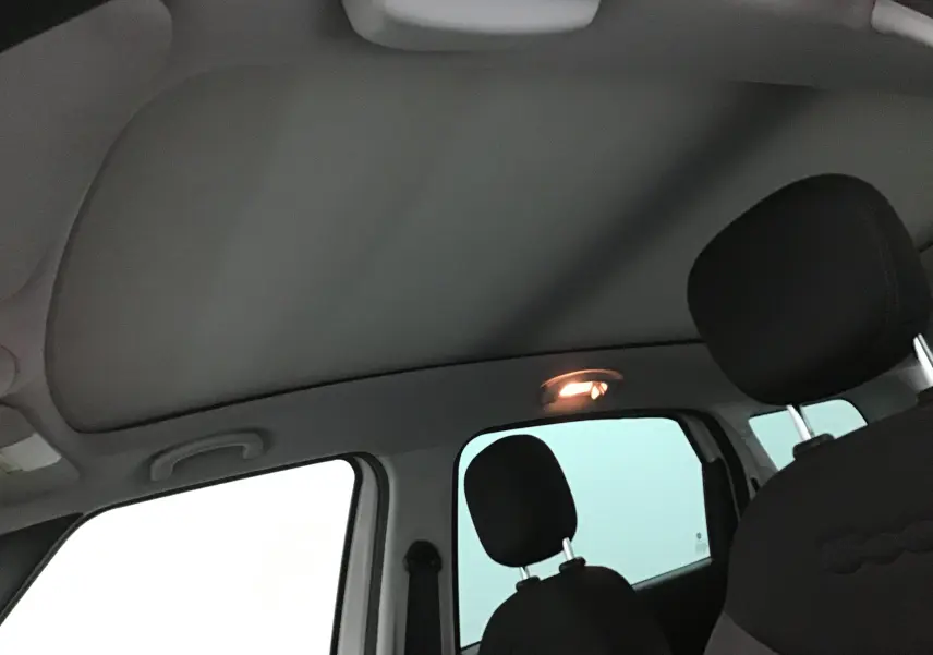 Vue intérieure du toit ouvrant et des sièges avant noirs d'une Fiat 500L blanche, version 7 places.