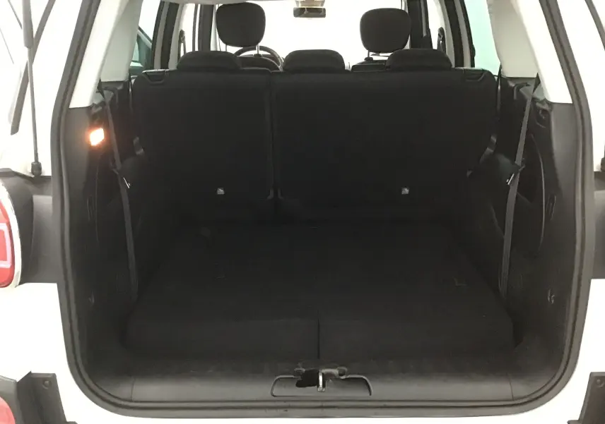 Coffre ouvert vu de l'arrière d'une FIAT 500L blanche, montrant les sièges arrière et l'espace de chargement.