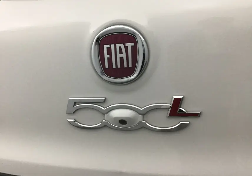 Gros plan sur le logo FIAT et l’inscription 500L chromée avec caméra de recul intégrée sur une carrosserie blanche.