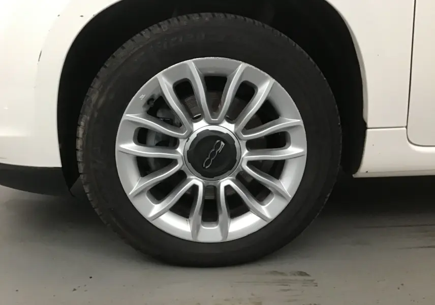 Gros plan sur la roue avant droite d'une FIAT 500L blanche, avec jante alliage argentée et logo central noir.