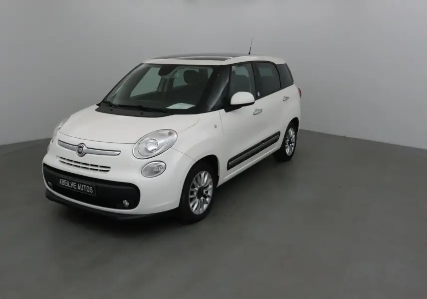 Vue 3/4 avant d'une Fiat 500L blanche avec toit panoramique et jantes alliage dans un studio gris.