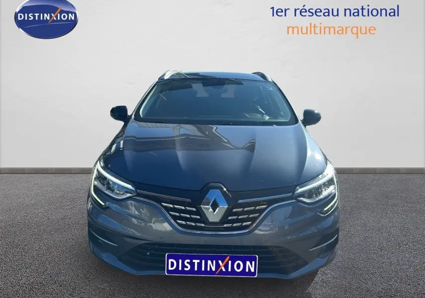 Vue frontale d'une Renault Mégane Break gris titanium métal avec calandre chromée et phares LED allumés.