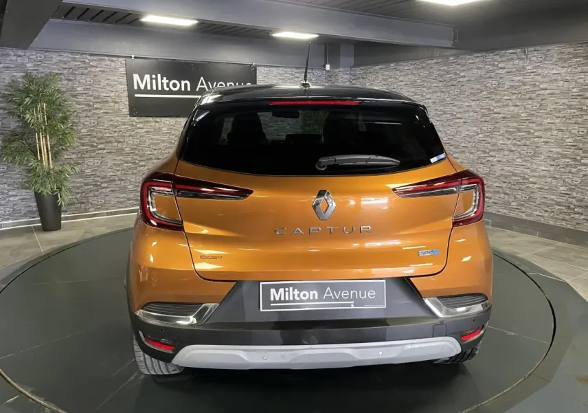 Vue arrière d'un Renault Captur orange avec toit noir, feux LED en forme de C et logo central sur fond intérieur gris.