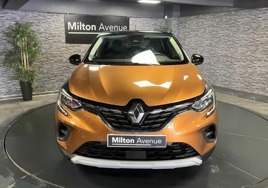 Vue frontale d'un Renault Captur orange avec calandre noire et détails chromés, en intérieur showroom.
