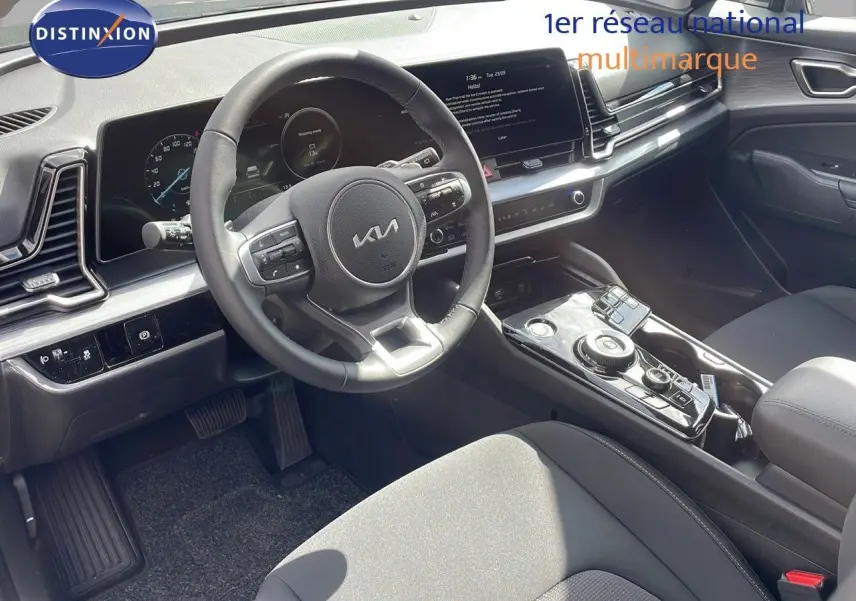 Intérieur du Kia Sportage 2025 vu côté conducteur, tableau de bord moderne avec écran tactile et volant multifonction noir.