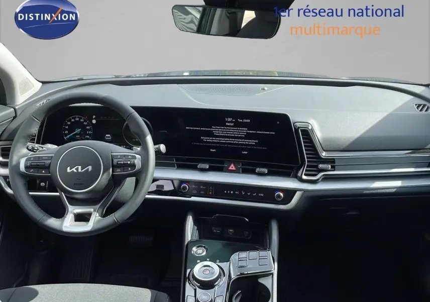 Vue intérieure du tableau de bord et volant du Kia Sportage 2025 gris foncé, avec écran tactile et commandes modernes.