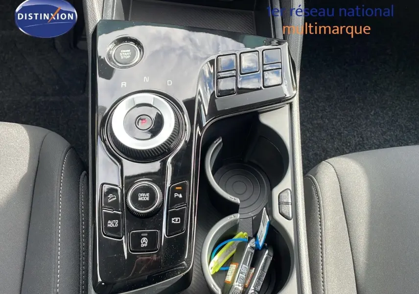 Vue plongeante sur la console centrale noire brillante du Kia Sportage 2025 avec molette de sélection et porte-gobelets.