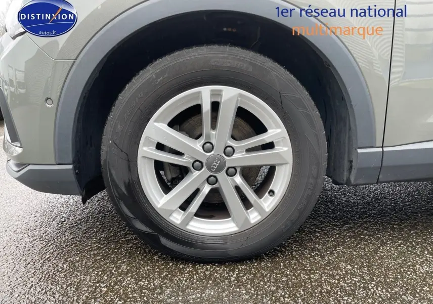 Gros plan sur la roue avant gauche d'un Audi Q3 gris Chronos métal, mettant en valeur la jante alliage 5 branches.