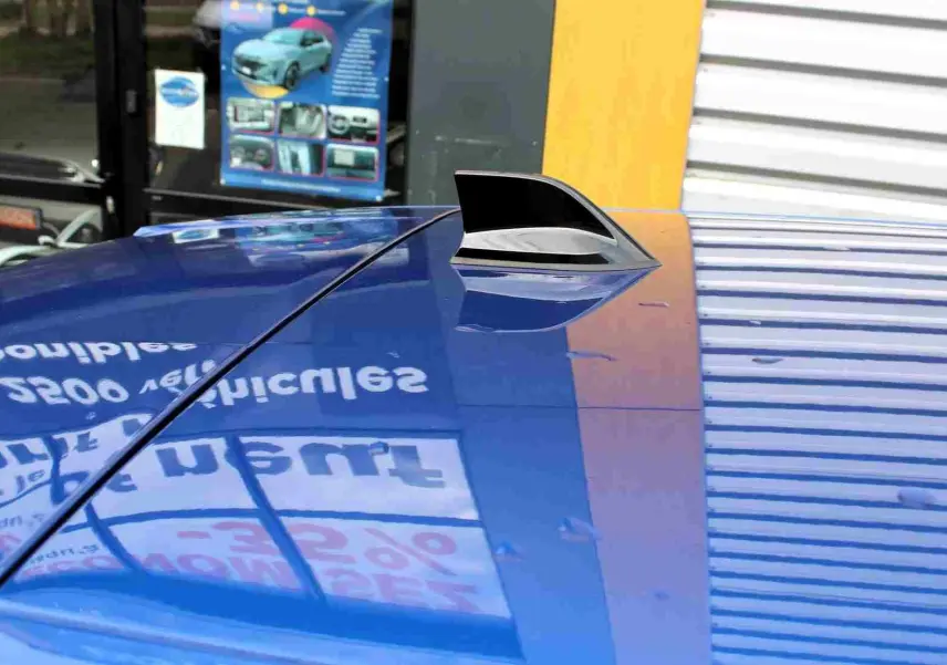 Gros plan sur l'antenne requin sur le toit bleu iron metal d'une Renault Symbioz 2025, reflet d'une enseigne visible.