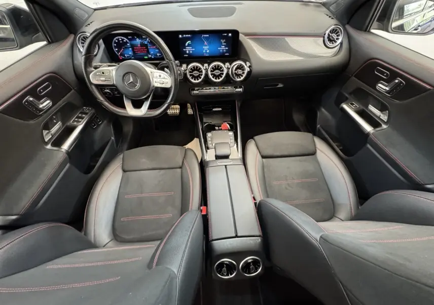 Vue intérieure avant de la Mercedes GLA 250 e AMG Line 2021, avec tableau de bord numérique et sièges noirs à surpiqûres rouges.