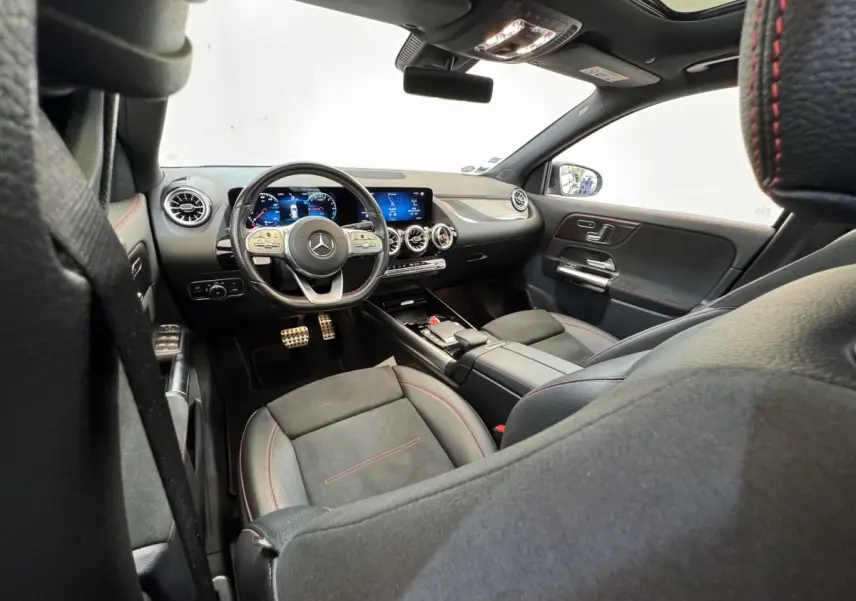 Vue intérieure avant droite de la Mercedes GLA 250 e AMG Line 2021, sièges noirs avec surpiqûres rouges et tableau de bord numérique.