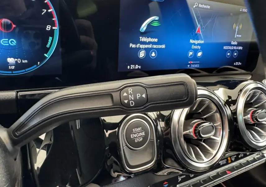 Gros plan intérieur sur la commande de boîte auto et le bouton Start Engine, avec écran tactile et aérateurs ronds chromés.