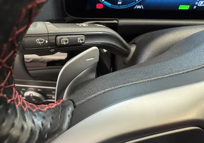 Gros plan sur la palette de changement de vitesse derrière le volant cuir noir avec surpiqûres rouges d'une Mercedes GLA 250 e AMG Line 2021.