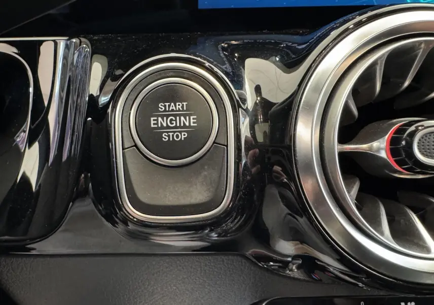 Gros plan sur le bouton start/stop moteur noir brillant et la sortie d'air circulaire chromée du tableau de bord Mercedes GLA 250 e AMG Line.