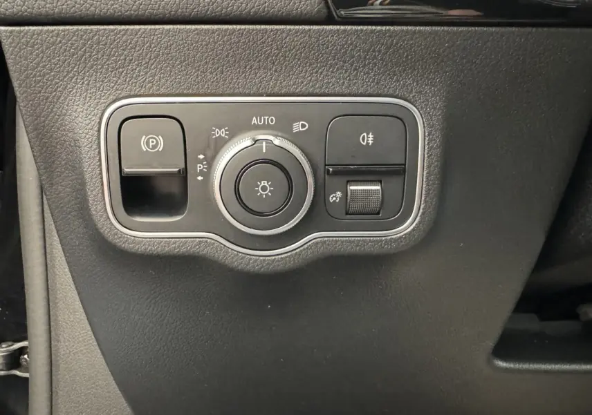 Gros plan sur le panneau de commande des phares et du frein à main électrique dans une Mercedes GLA 250 e AMG Line noire.