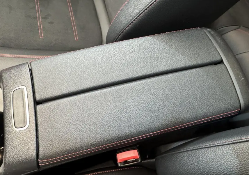 Gros plan sur l'accoudoir central en cuir noir avec surpiqûres rouges, sièges en tissu noir partiellement visibles.