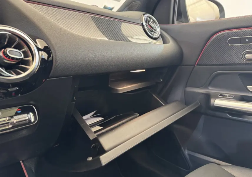 Vue intérieure côté passager du tableau de bord noir avec boîte à gants ouverte et aérateurs ronds du Mercedes GLA 250 e AMG Line.
