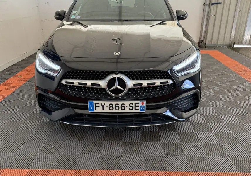 Vue avant d'une Mercedes GLA 250 e AMG Line noire, avec calandre étoilée et phares LED allumés dans un garage.
