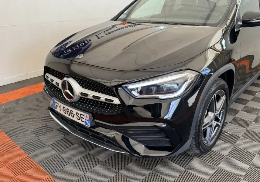 Vue 3/4 avant droit d'une Mercedes GLA 250 e AMG Line noire, avec calandre étoile et phares LED distinctifs.