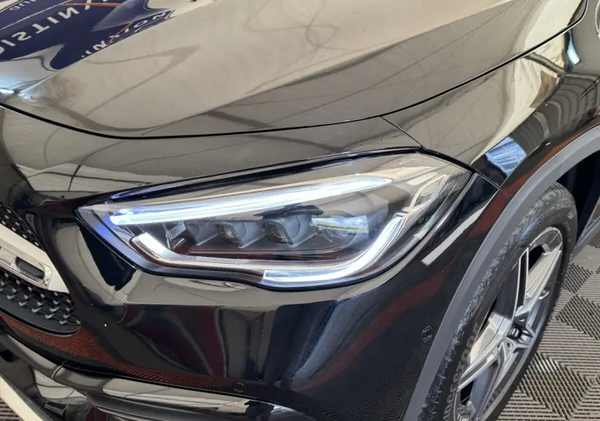 Gros plan sur le phare avant droit et la roue d’une Mercedes GLA 250 e AMG Line noire, finition brillante.