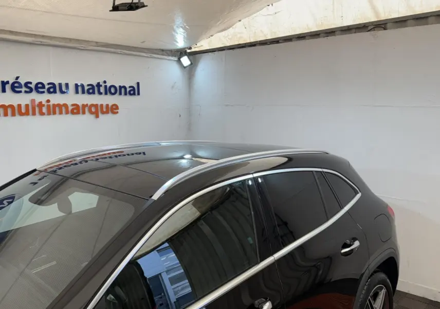 Vue 3/4 arrière droite d’un Mercedes GLA 250 e AMG Line noir avec vitres teintées et barres de toit chromées dans un showroom.