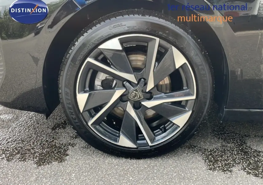 Gros plan sur la roue avant gauche d’une Peugeot 308 SW Hybrid noire métal avec jante alliage bicolore distinctive.