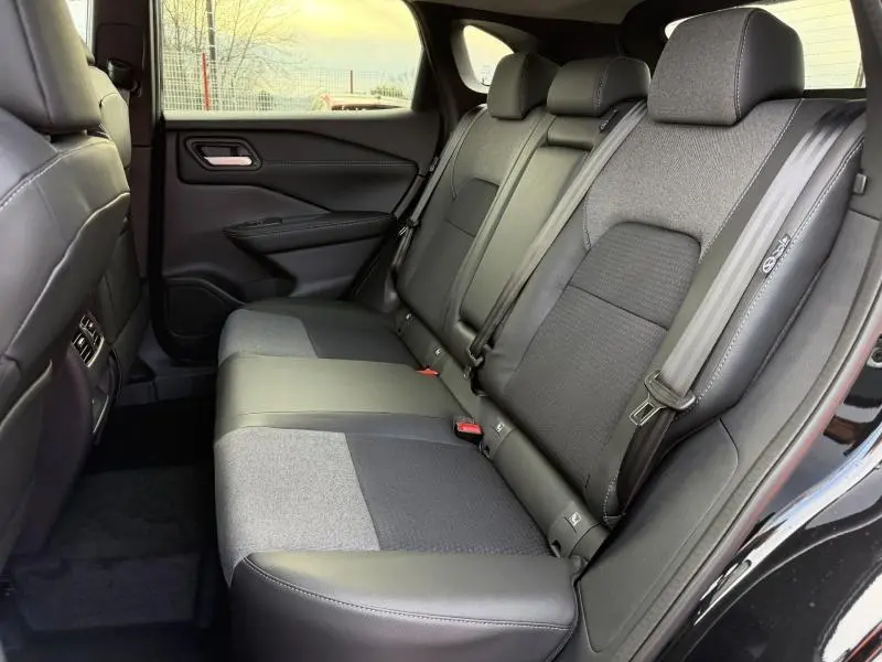 Vue intérieure côté gauche des sièges arrière en tissu gris et noir du Nissan Qashqai Hybrid e-POWER 2025, avec ceinture de sécurité visible.