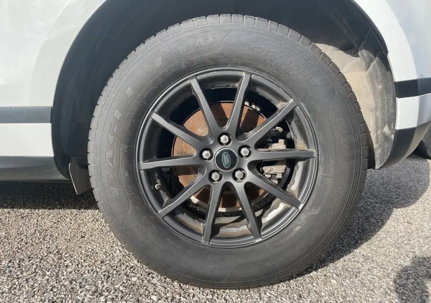 Gros plan sur la roue avant droite d'un Range Rover Evoque blanc 2020 avec jante noire et logo Land Rover central.