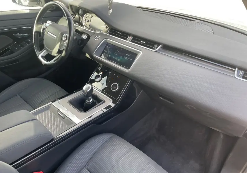 Vue intérieure côté conducteur du Range Rover Evoque 2020 blanc, mettant en valeur la console centrale avec boîte manuelle et écran tactile.