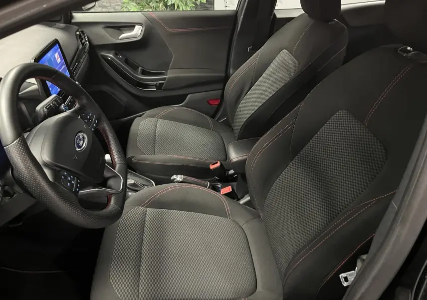 Vue intérieure côté conducteur du Ford Puma noir 2023, sièges tissu noir avec surpiqûres rouges et volant ST-Line.