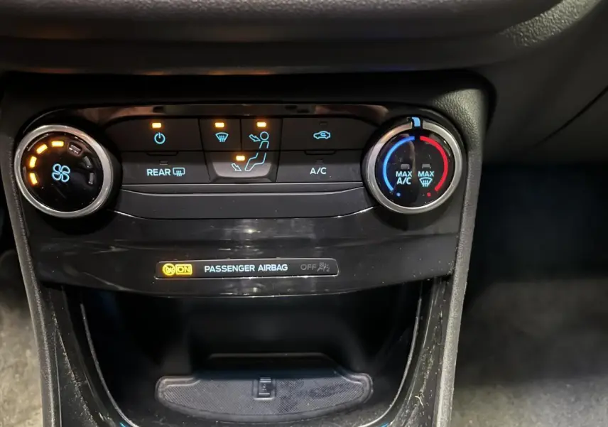 Vue rapprochée de la console centrale du Ford Puma noir 2023, montrant les commandes de climatisation et l'indicateur airbag passager.