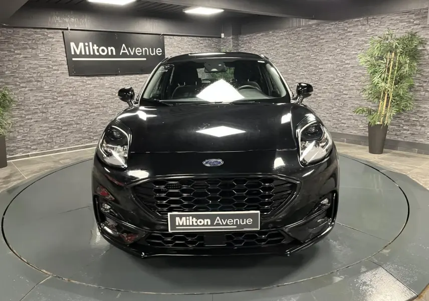 Vue frontale d'un Ford Puma noir brillant avec calandre hexagonale et phares LED dans un showroom.