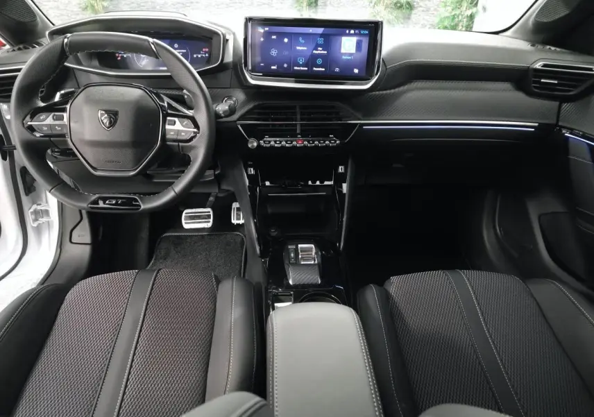 Vue intérieure avant de la Peugeot 208 blanche 2025, volant compact GT, écran tactile central et sellerie noire.