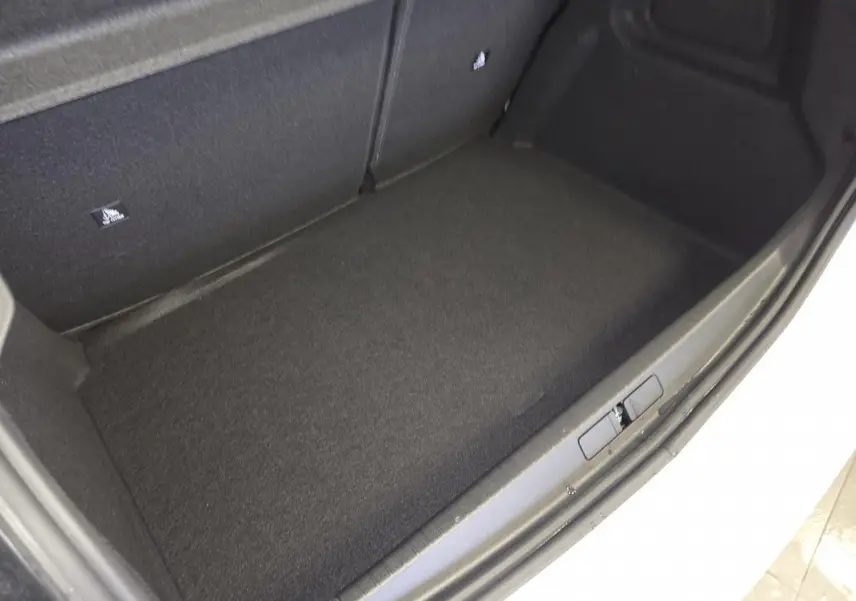 Vue rapprochée du coffre noir d’une Peugeot 208 blanche hybride, montrant le tapis de sol et la bordure du coffre.